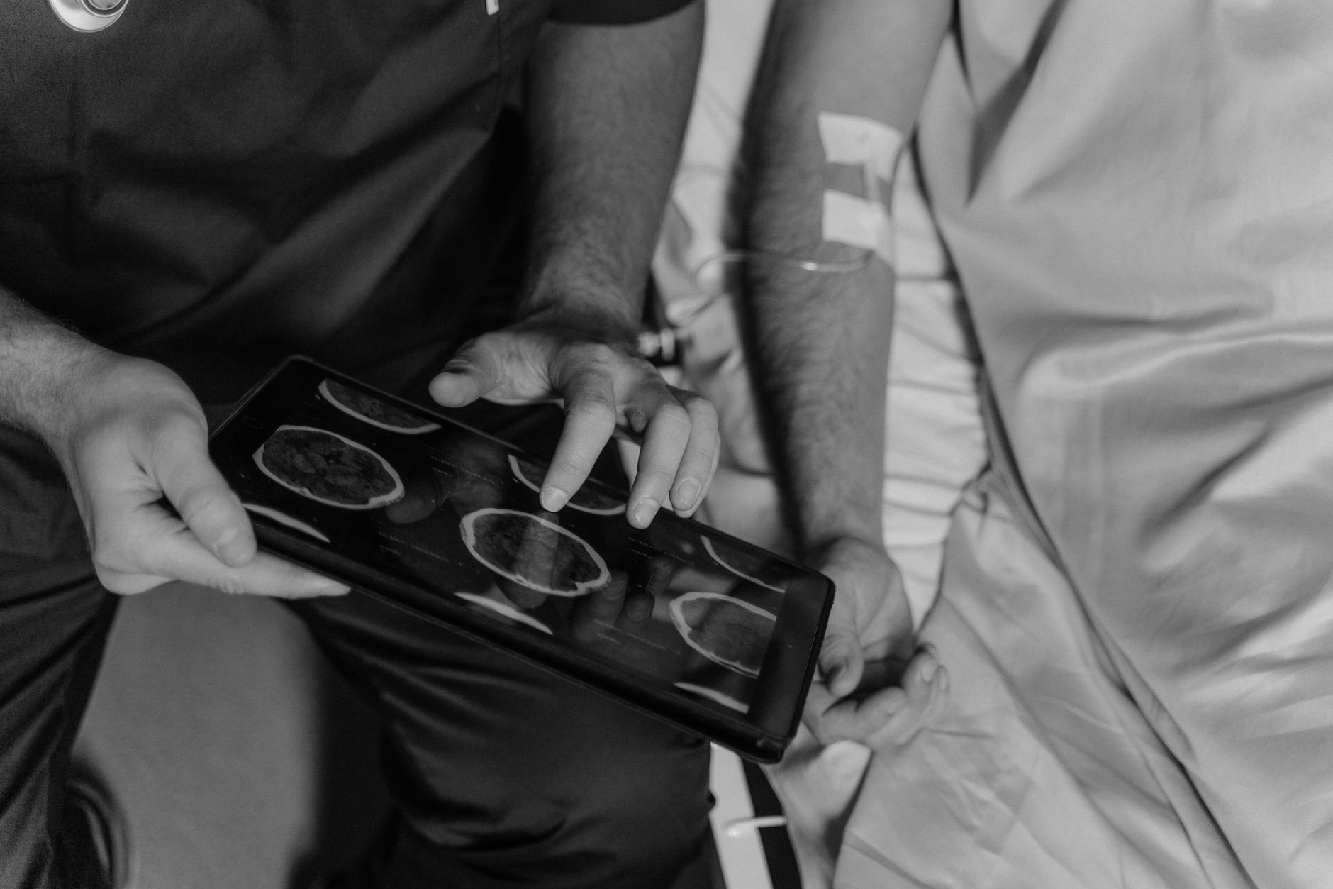 Medical professional reviews patient's CT scans on a digital tablet in grayscale.