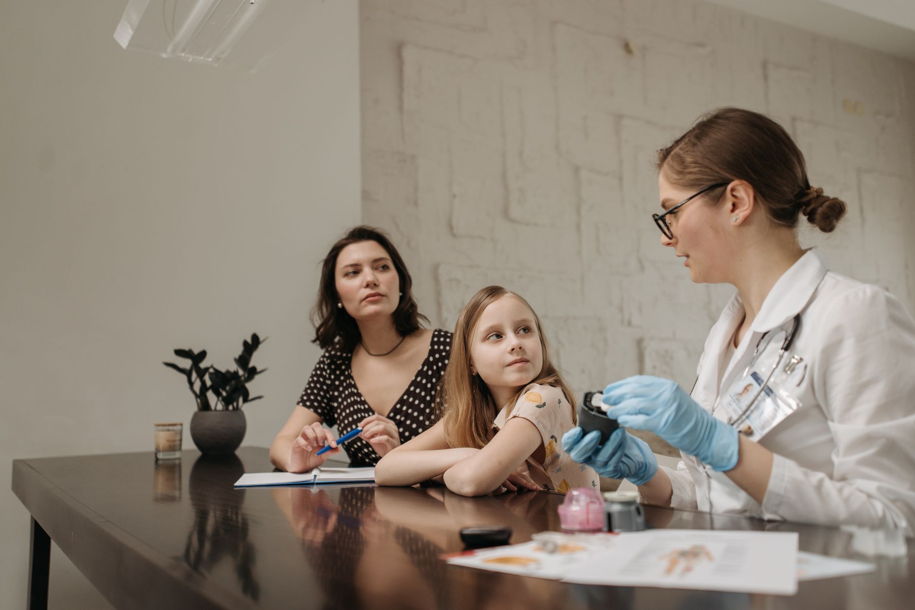 A doctor in a white coat consults a young girl and her mother about health in an indoor setting.