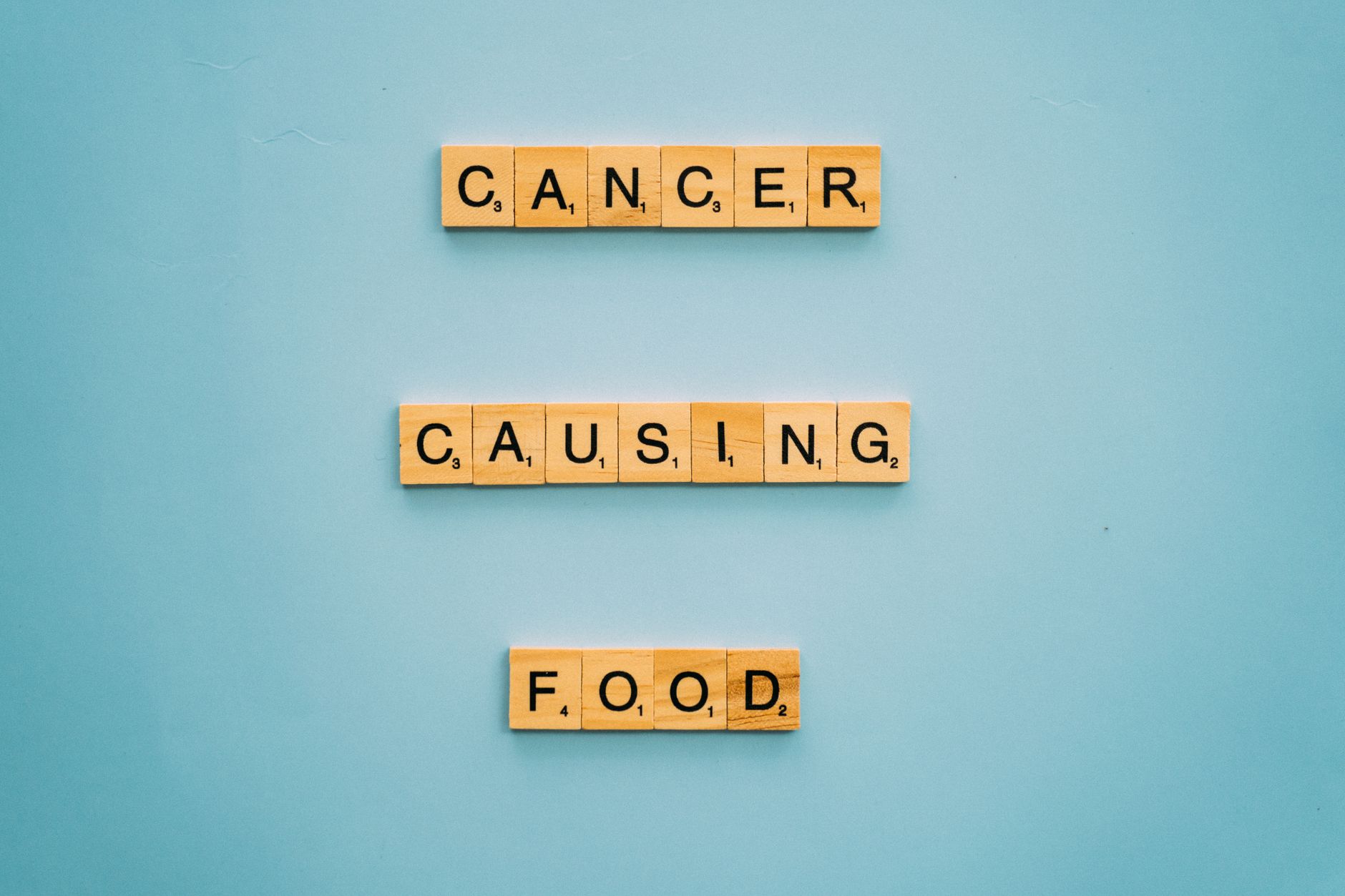 Conceptual image showing words 'cancer causing food' on Scrabble tiles against a blue background.