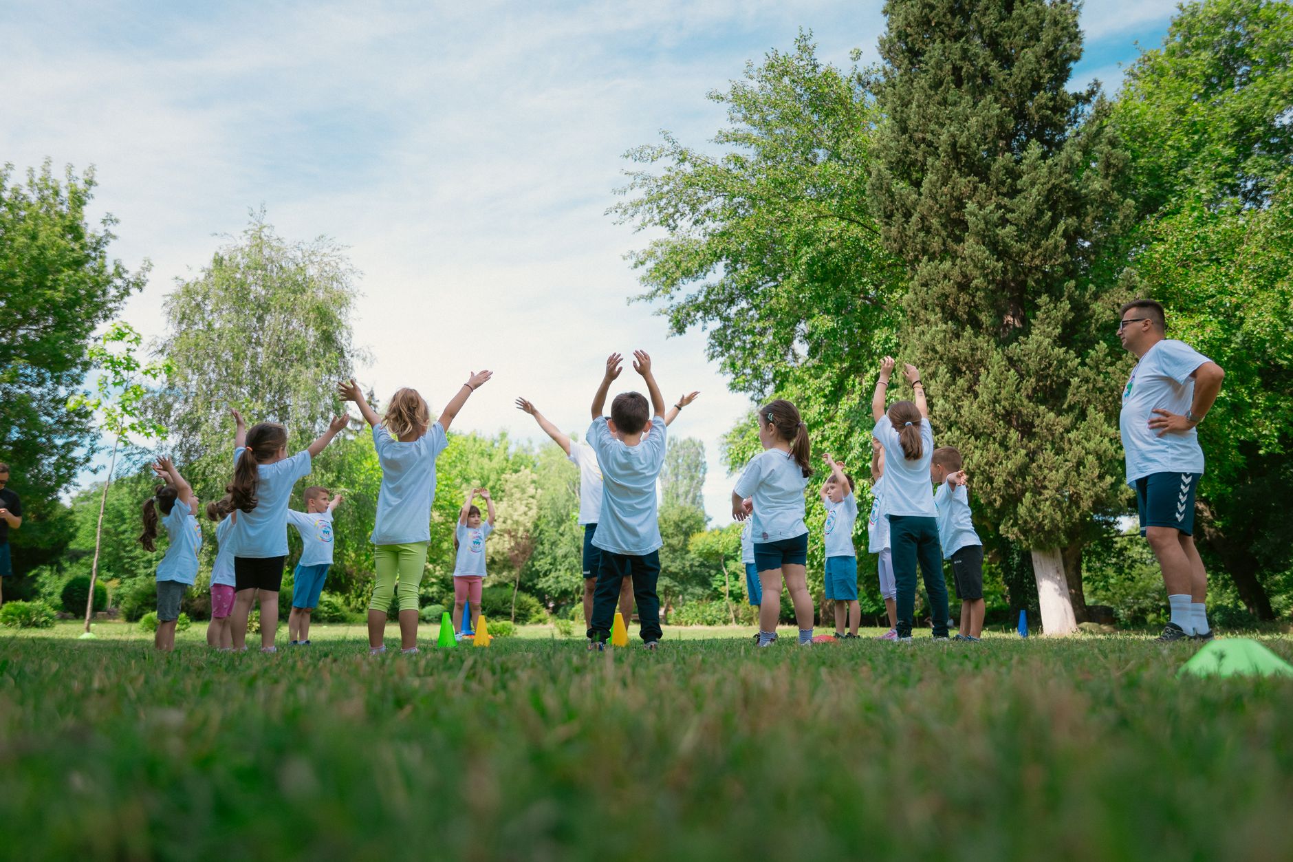 Group of children with instructor doing exercises in a sunny park setting, promoting outdoor activity.