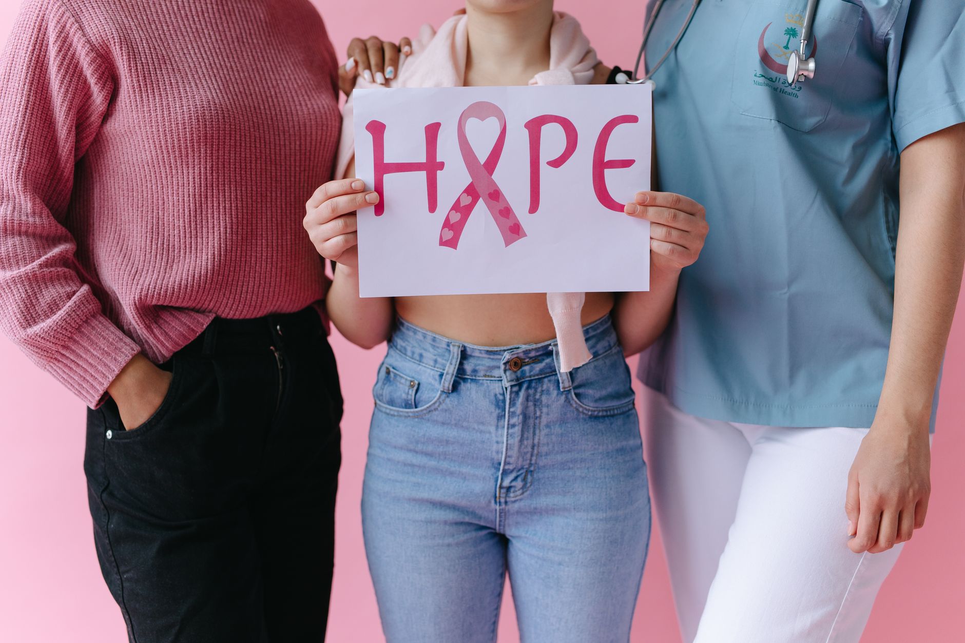 Three women holding a 'HOPE' sign with a pink ribbon for breast cancer awareness.