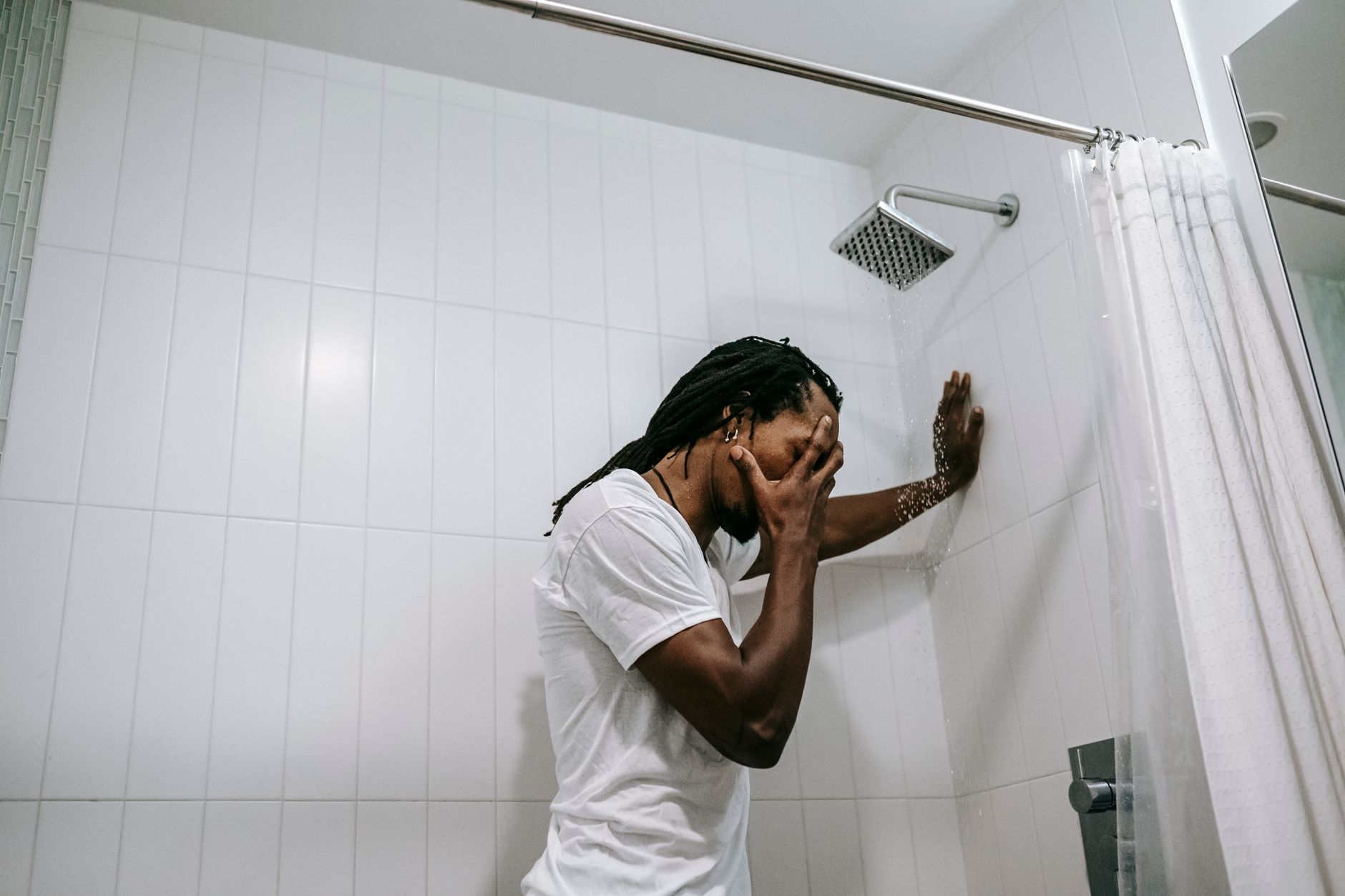 Side view depressed preoccupied African American male in white shirt covering face with hand in anxiety in bathroom