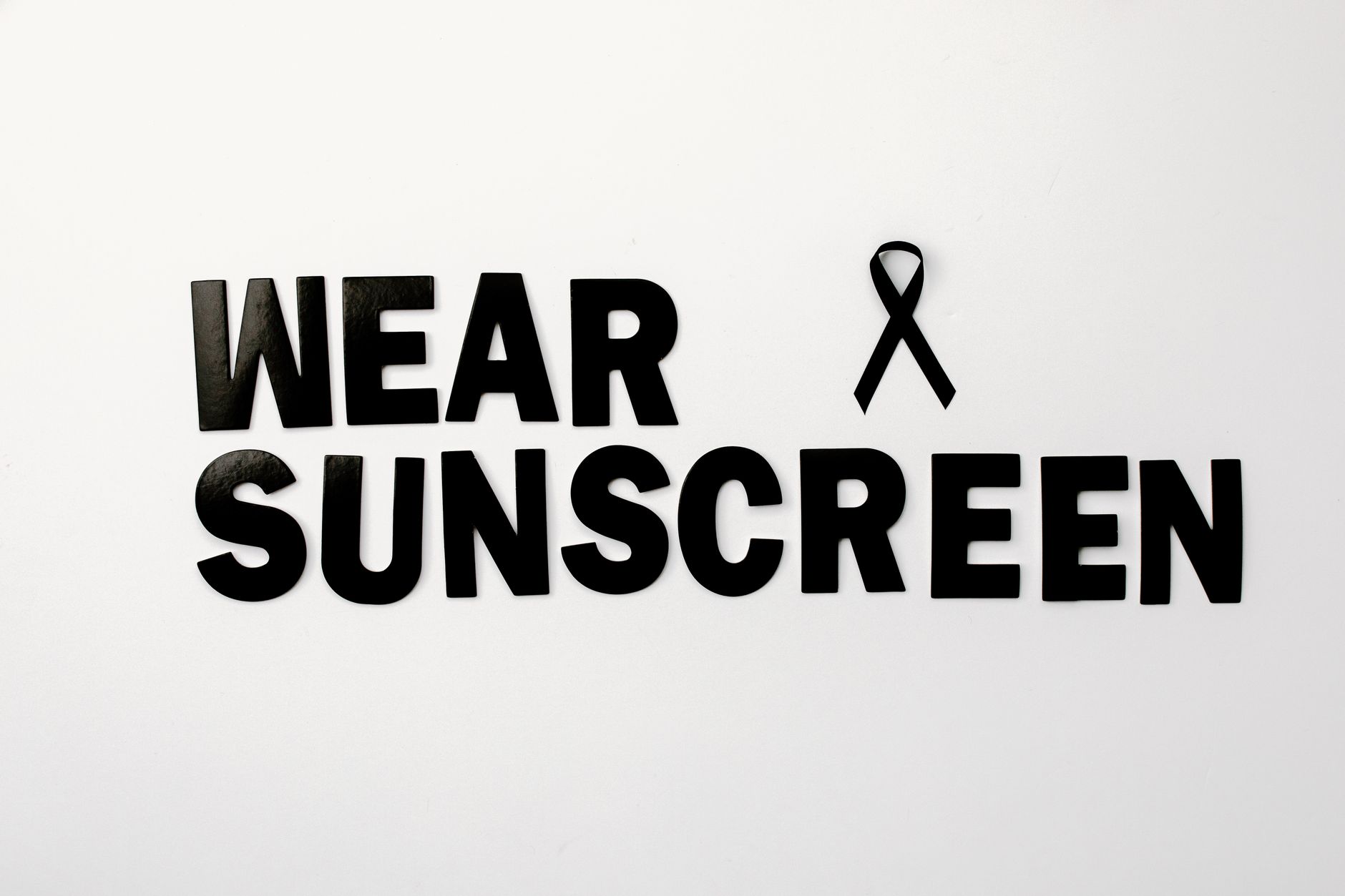 Black text and ribbon promoting skin cancer awareness with a sunscreen message.