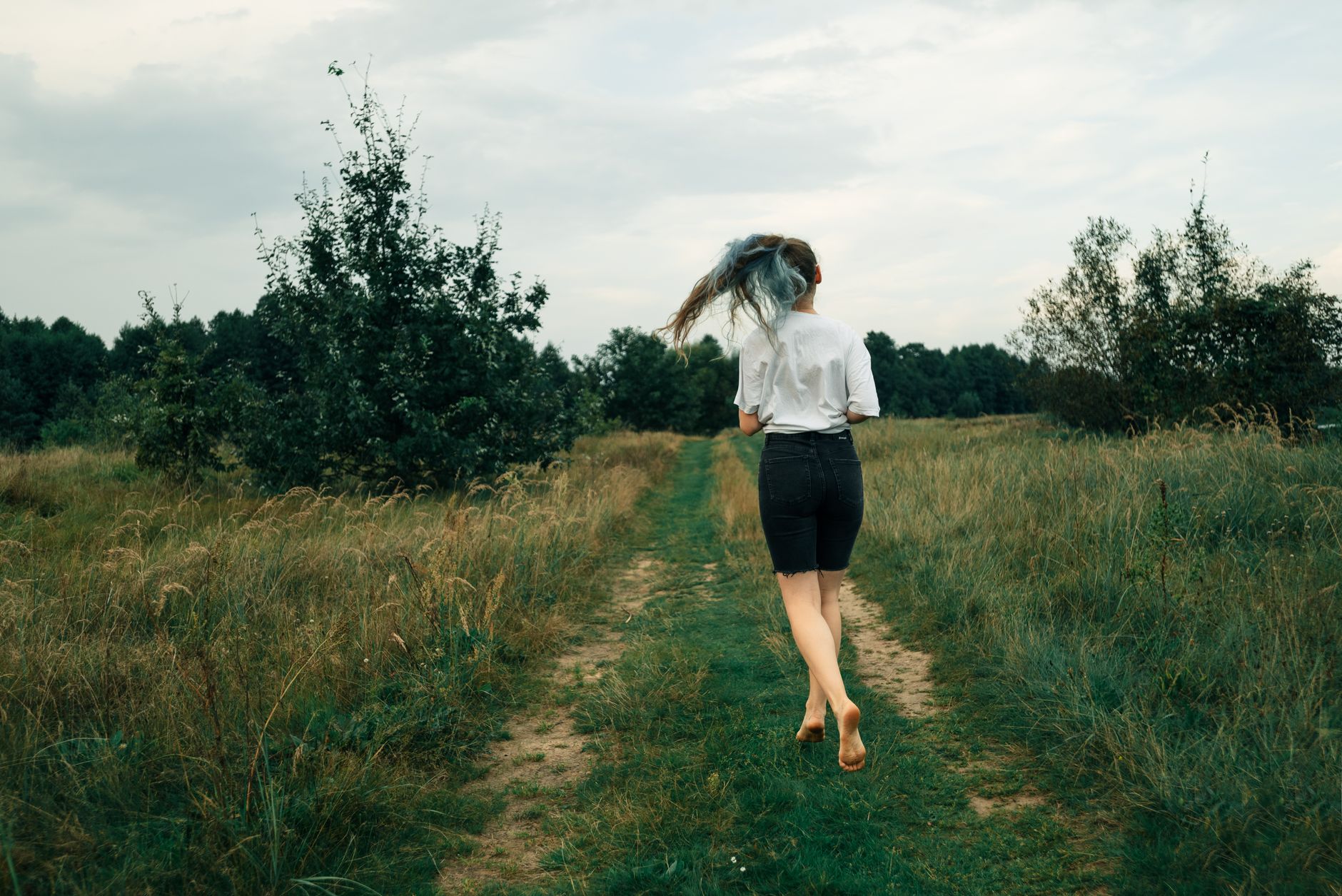 A woman joyfully runs through a lush green field, embracing the outdoors.