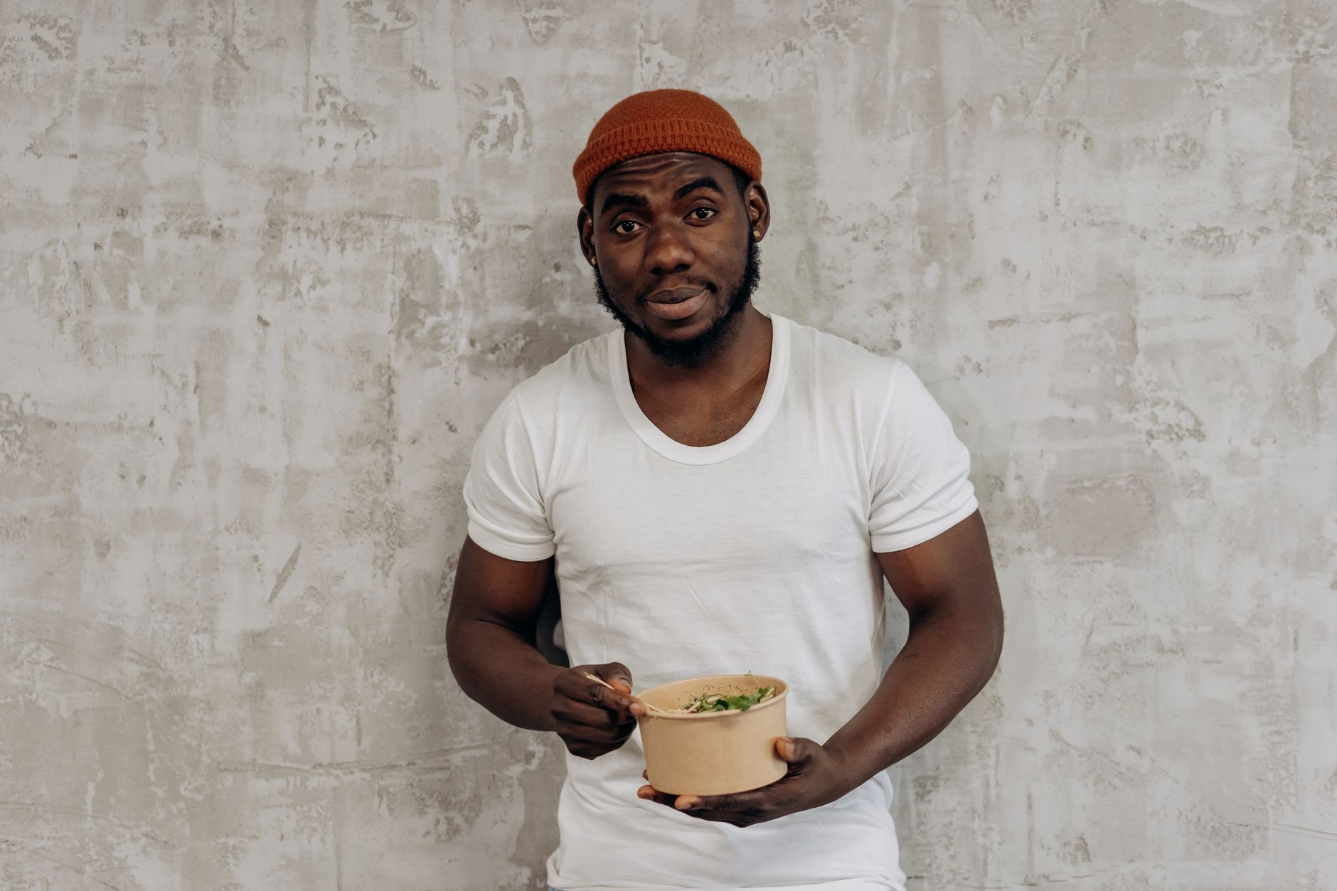 Smiling man in a white t-shirt enjoying a healthy meal indoors, embodying a fit lifestyle.