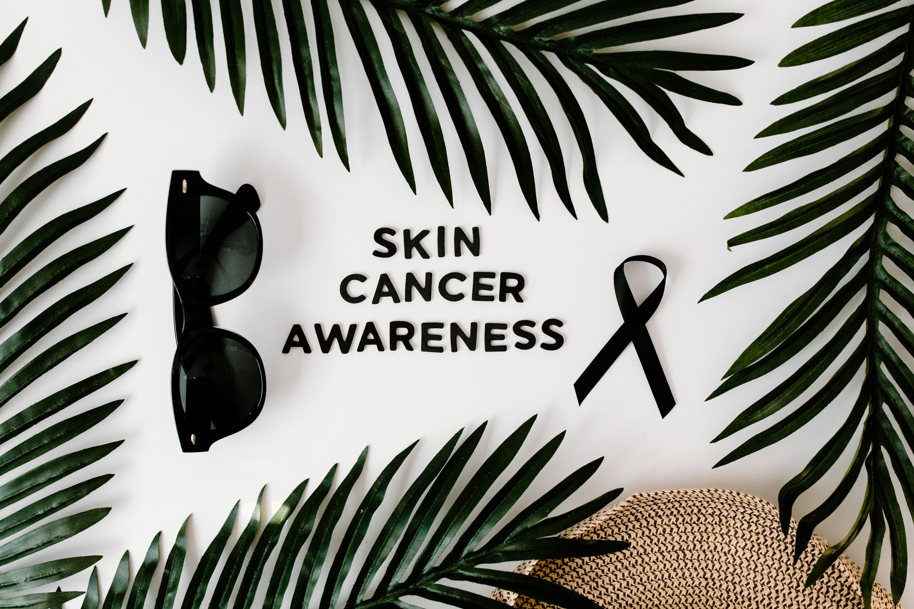 Flat lay promoting skin cancer awareness with sunglasses, black ribbon, and foliage.