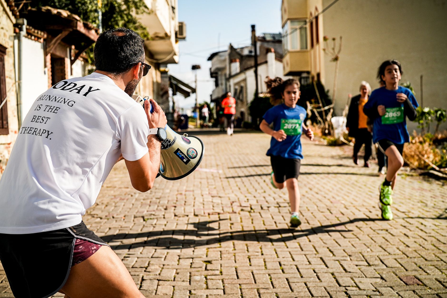 Children running a street race while a man with a megaphone cheers them on.