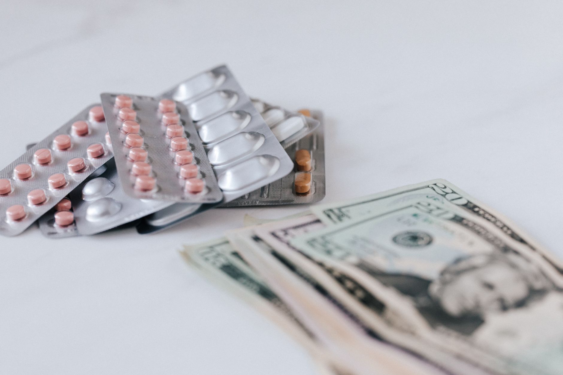 Multicolored pills in silver blisters on white surface near heap of paper money representing expensive pharmacy