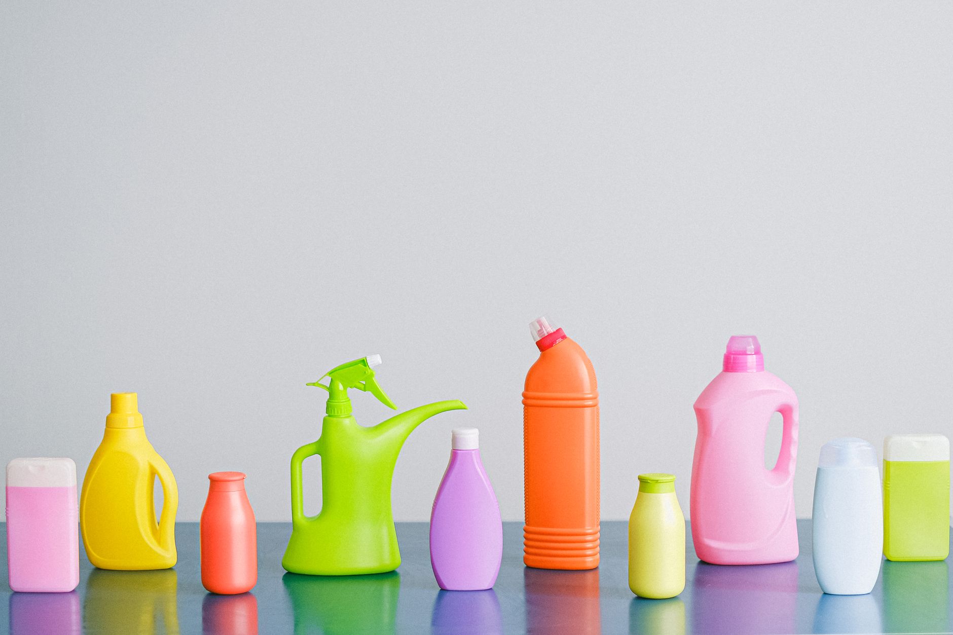 Arrangement of colorful plastic bottles with assorted cleaning products for household placed on table in row against white background in lig