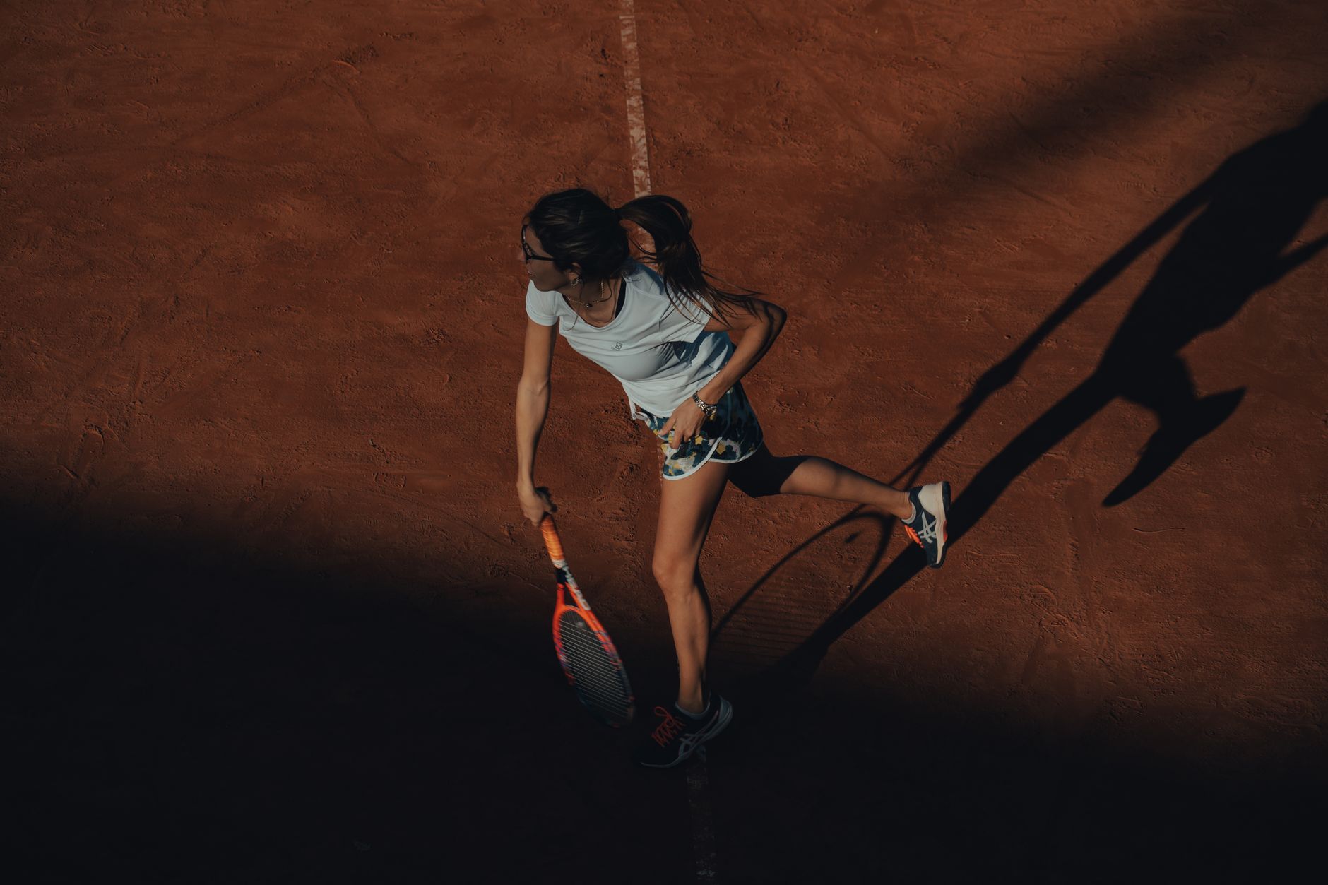 A female tennis player in action on a clay court, captured during a dynamic moment.