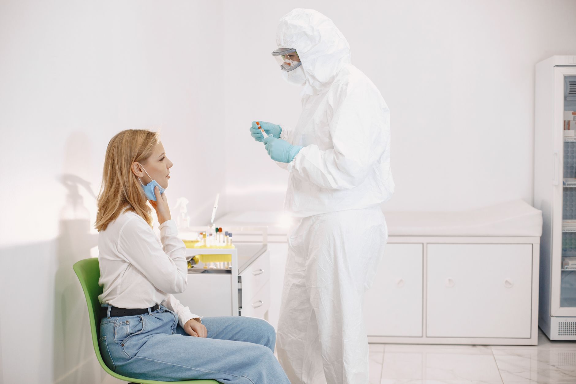 Medical professional in PPE collecting a swab sample from a patient in a clinical setting.