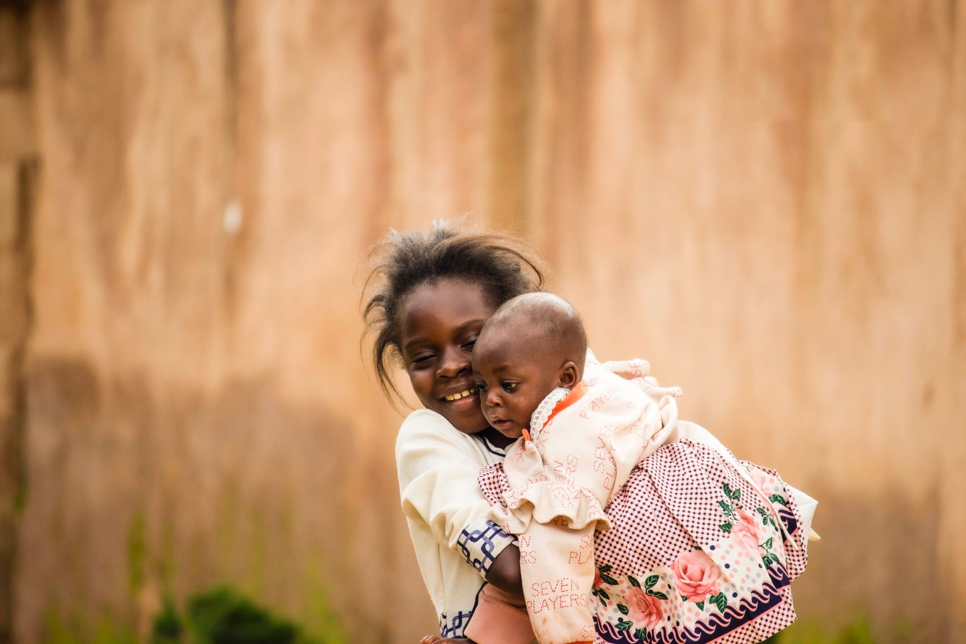 A heartwarming outdoor portrait of an older child holding a baby sibling, showcasing affection and joy.