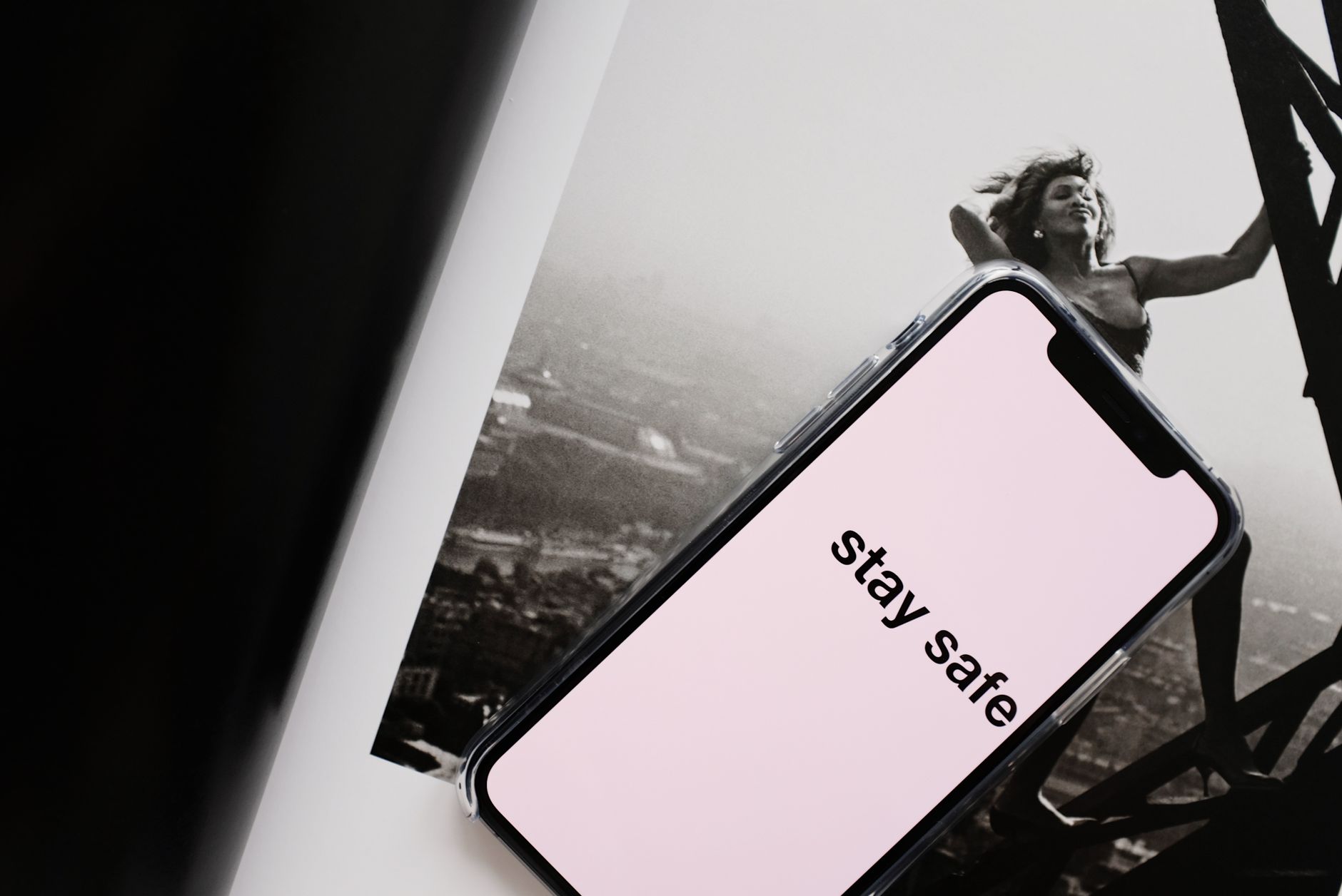 From above of cellphone with pale pink screen and STAY SAFE inscription put on open magazine with image of cheerful female climbing metal to