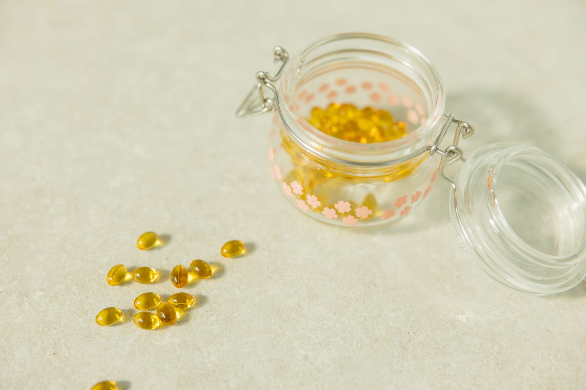 Close-up of open glass jar filled with yellow health capsules on light surface.