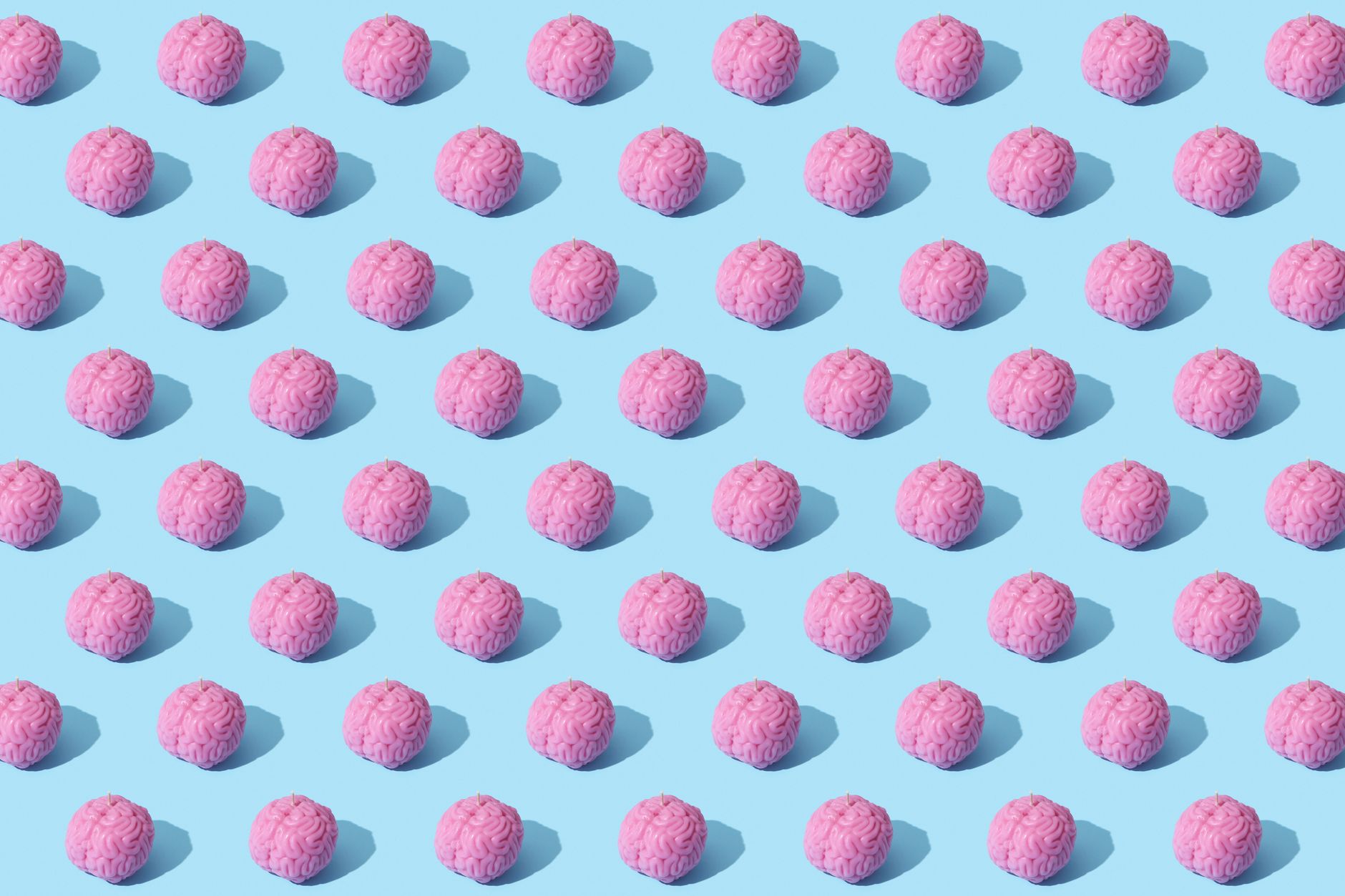 Creative composition of pink brain models in a repeating pattern on a light blue surface, showcasing abstract thinking.