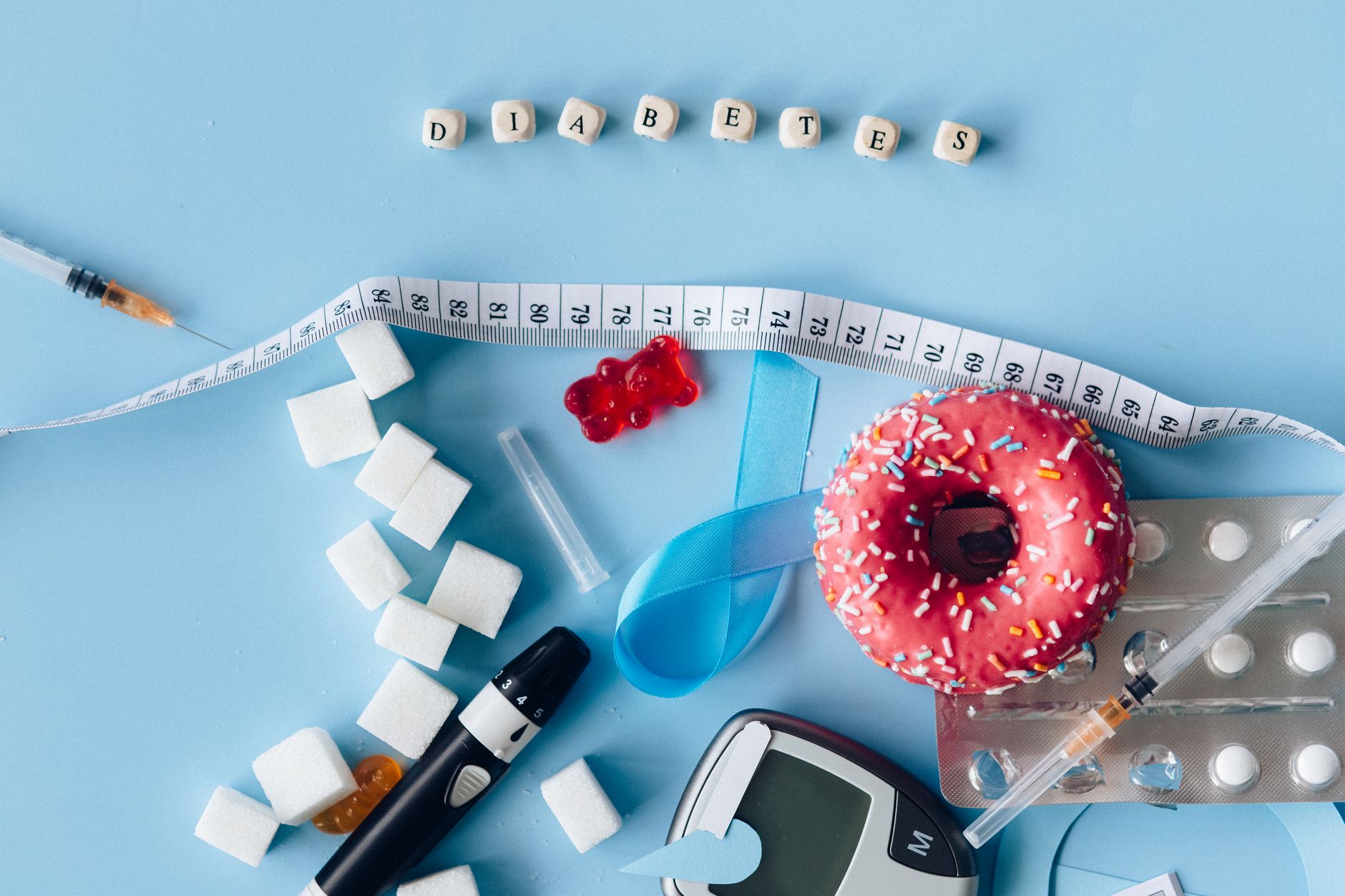 Flat lay of diabetes awareness concept with glucose meter, insulin syringes, sugar cubes, and donut.