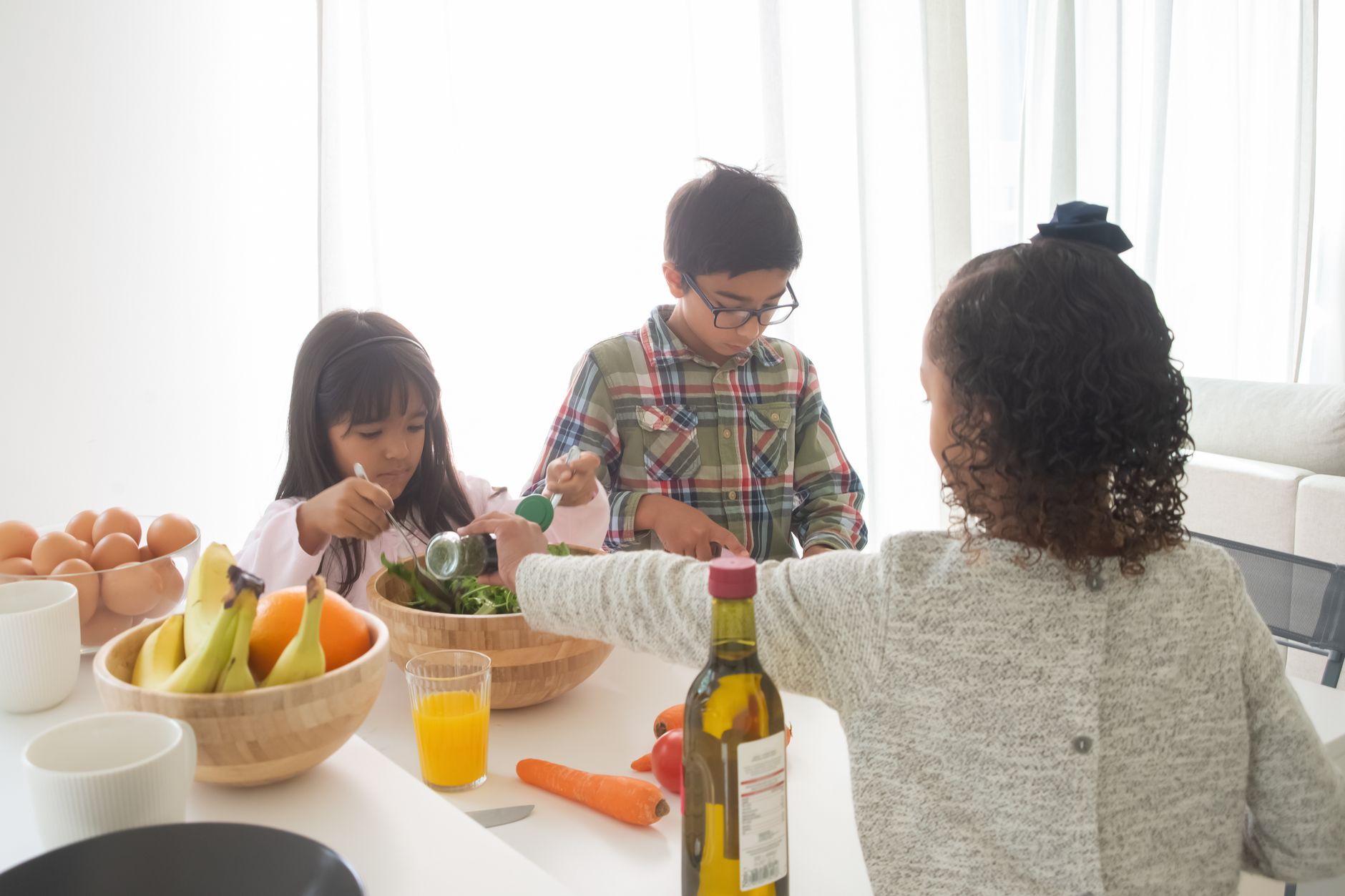 Three children making a fresh salad together in a modern, bright kitchen setting.