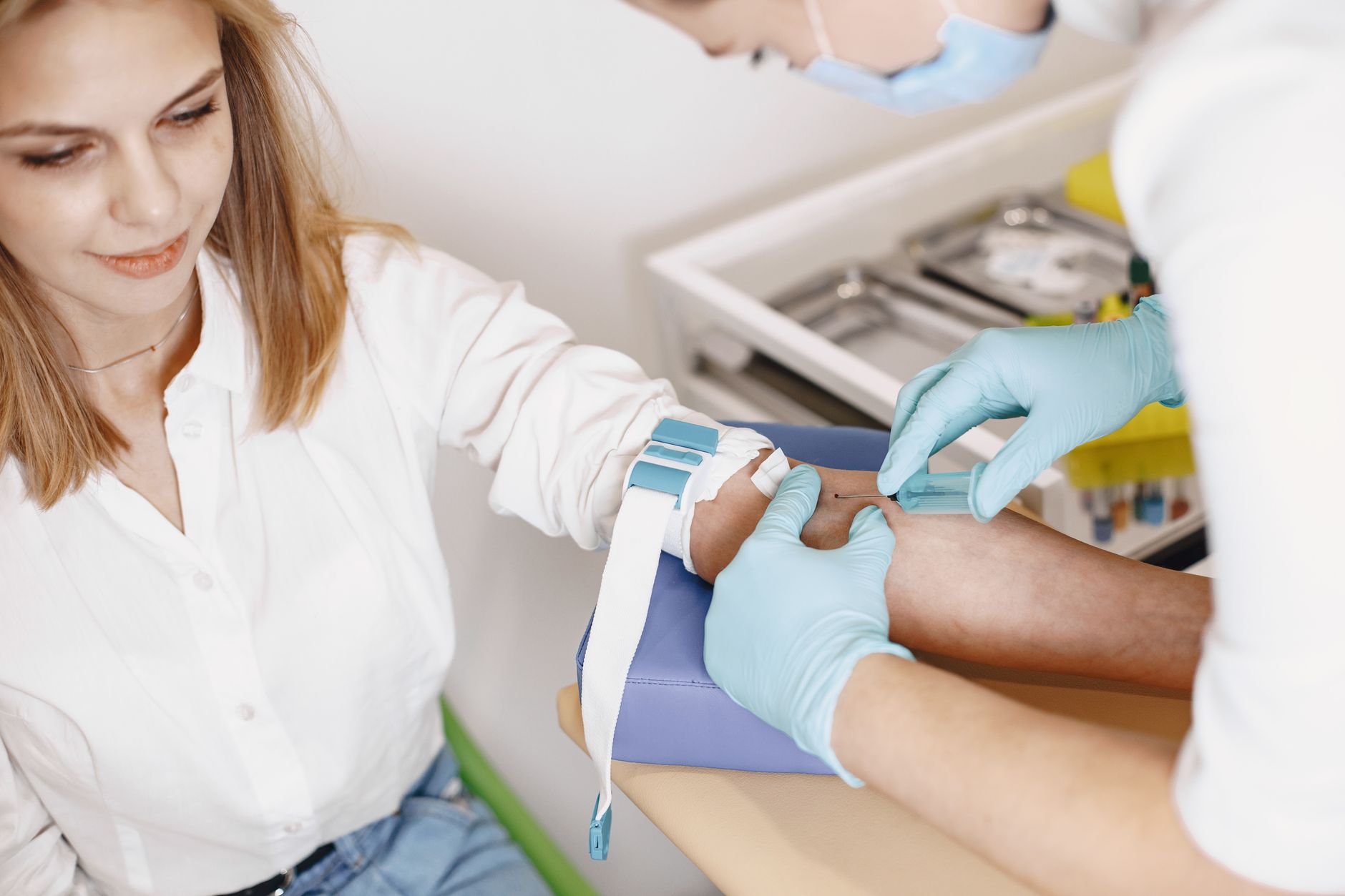 A nurse prepares a female patient for a blood test in a clinical setting, illustrating healthcare procedures.