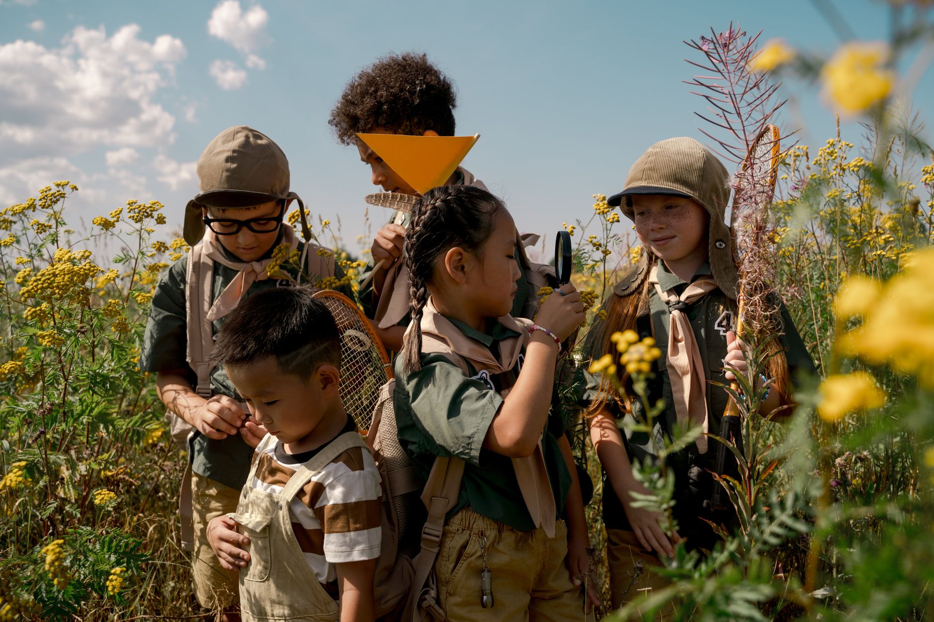 A diverse group of children engaged in scouting activities amidst a summer field of wildflowers.