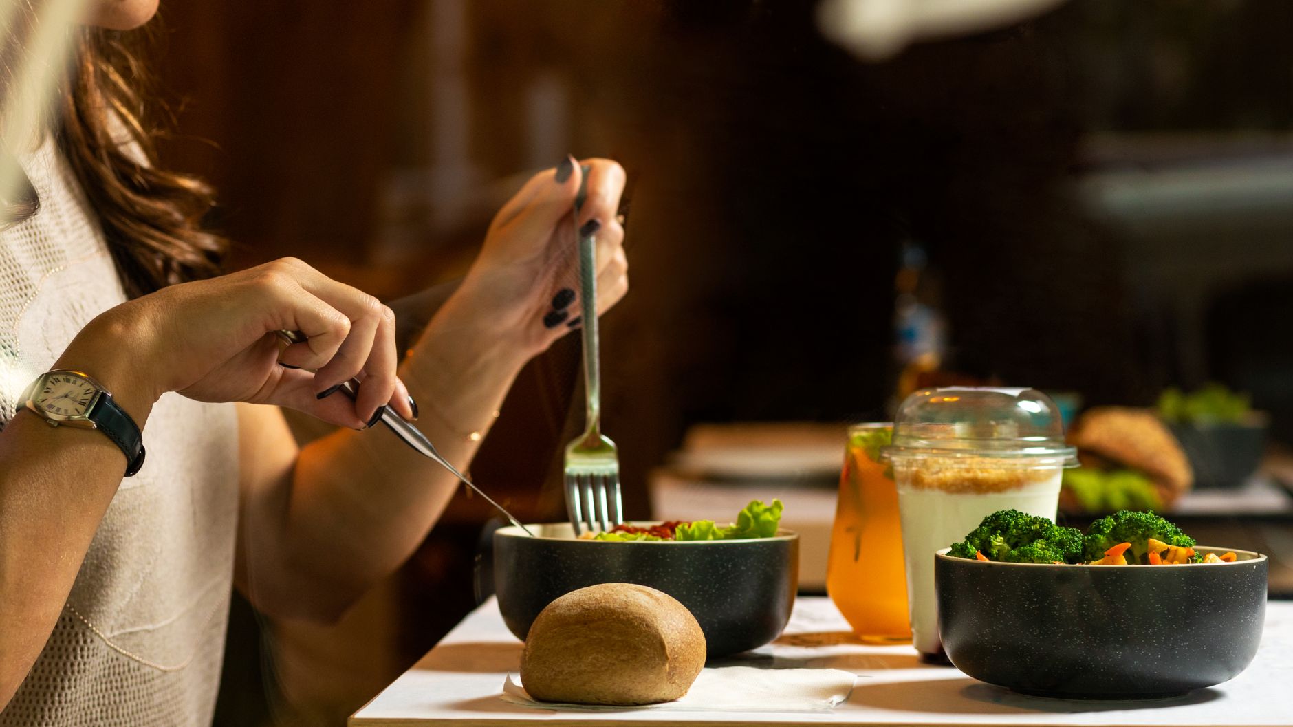 A woman dining on a fresh salad with vegetables and a drink indoors.