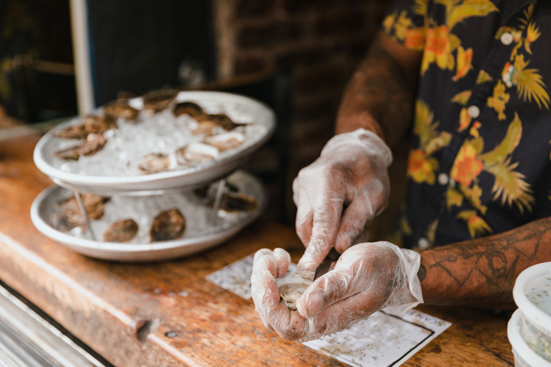 A man in gloves skillfully shucking oysters at a seafood bar, showcasing fresh seafood.