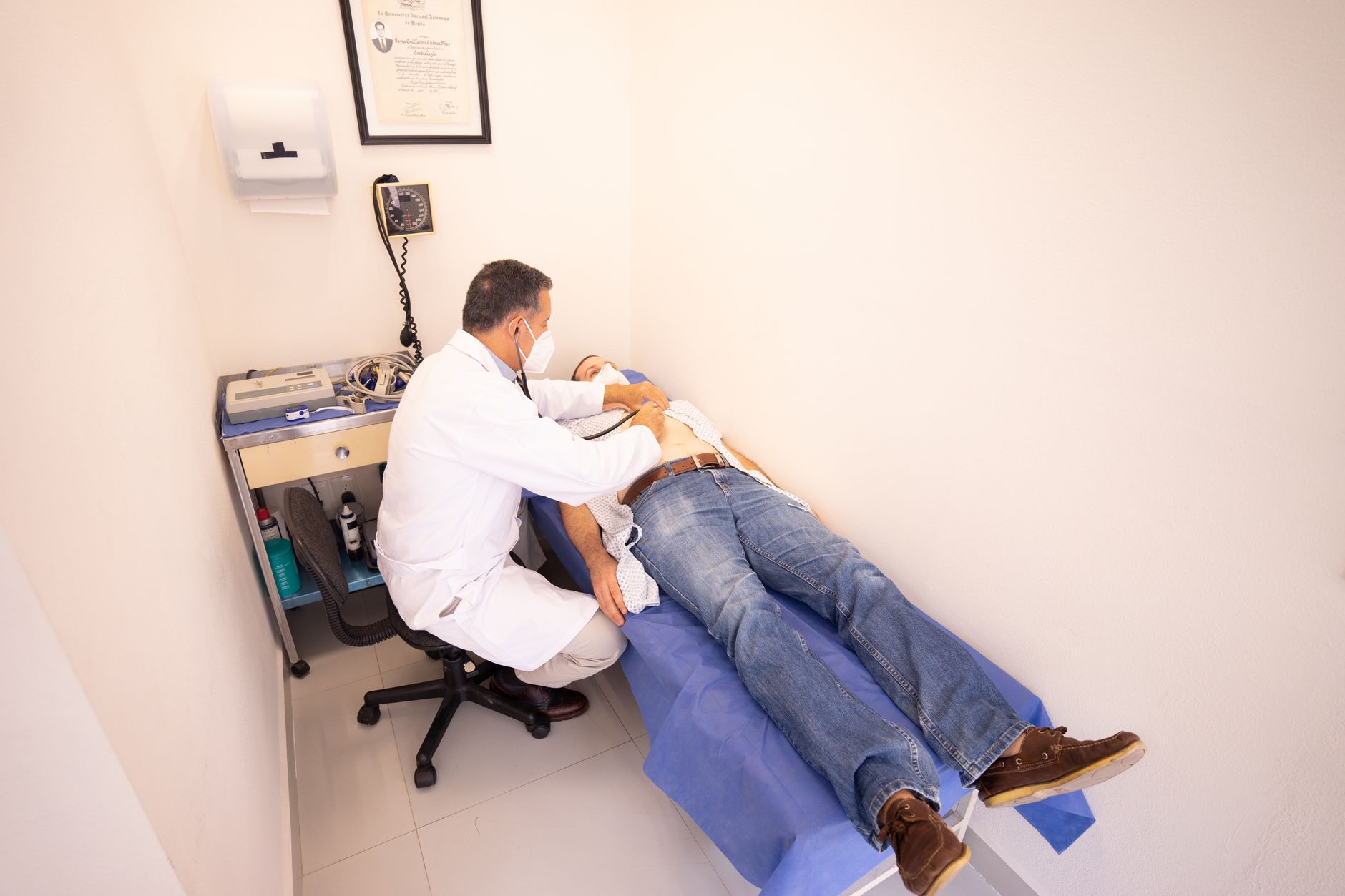 Medical professional examines patient with stethoscope in clinic examination room.