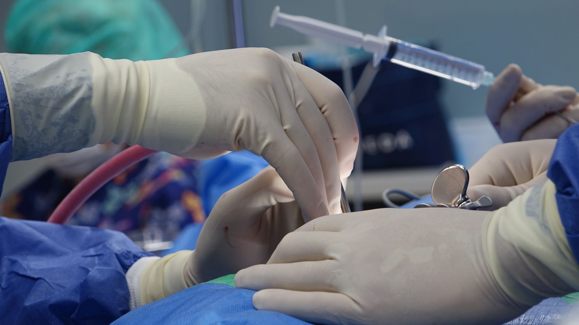 Close-up of surgeons' hands performing a delicate procedure with syringe and medical tools in a sterile operating room.