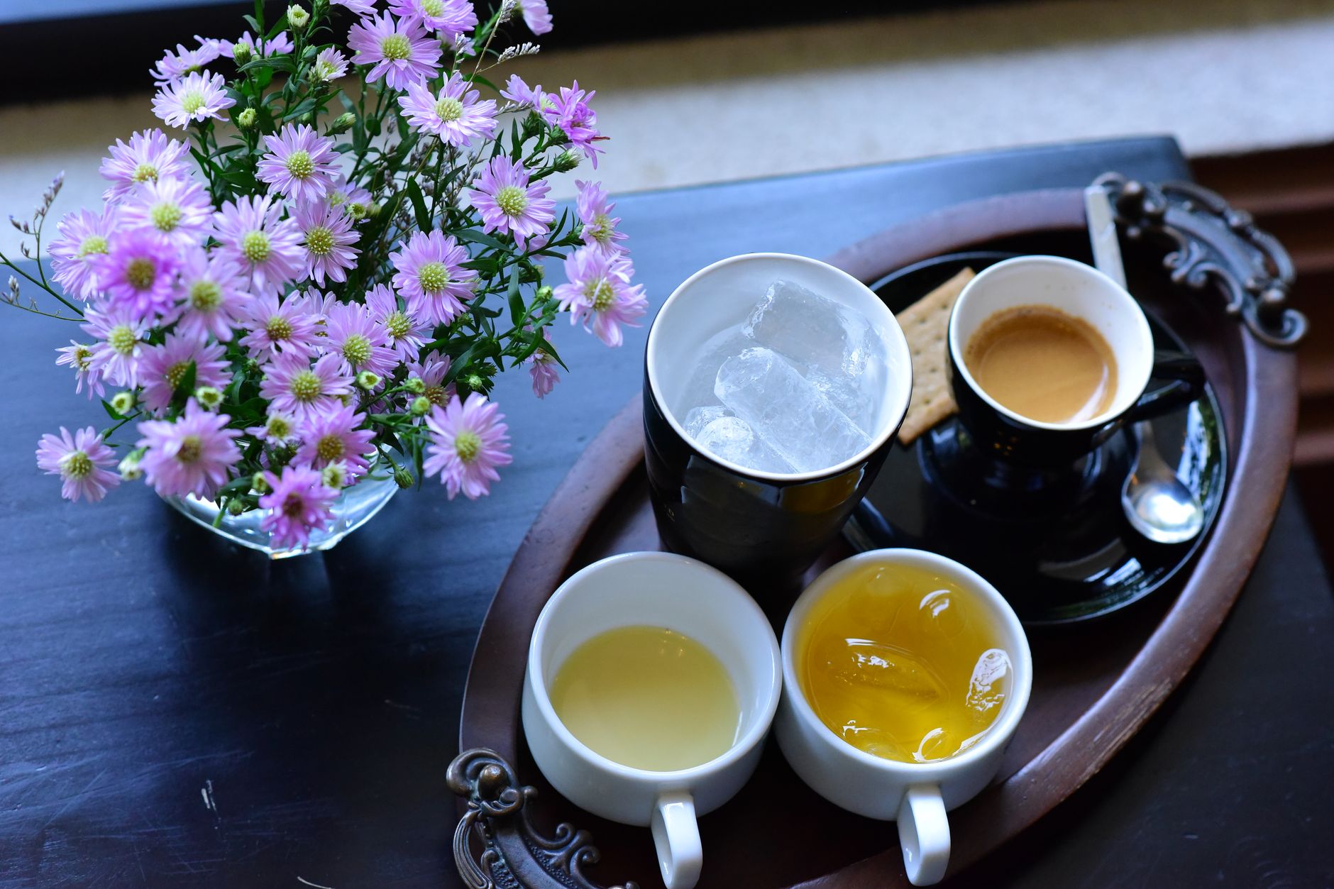 A stylish arrangement of coffee, tea, and flowers on a dark wooden tray.