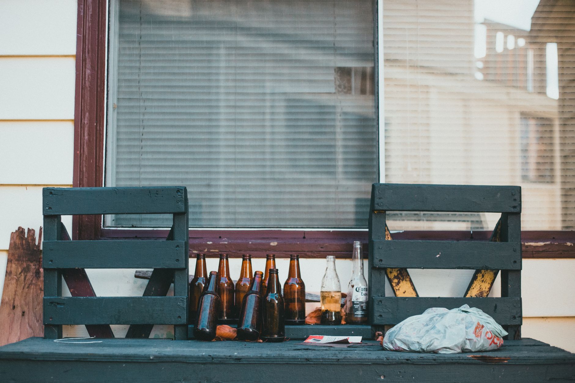 A collection of empty beer bottles on a rustic outdoor bench, amidst casual clutter.