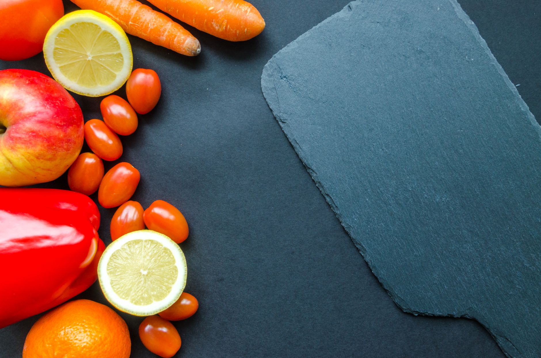 Vibrant fresh fruits and vegetables on a dark slate background with ample copyspace.