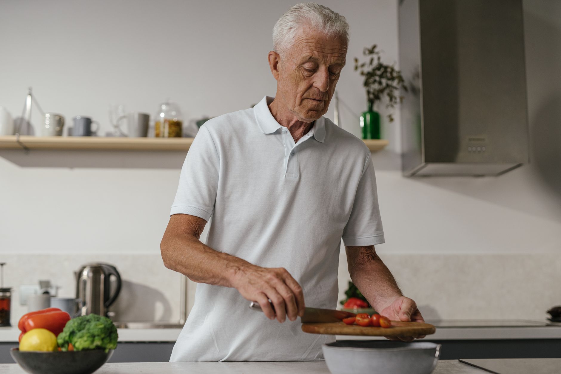 Senior man slicing vegetables in contemporary kitchen setting, focused on healthy cooking.
