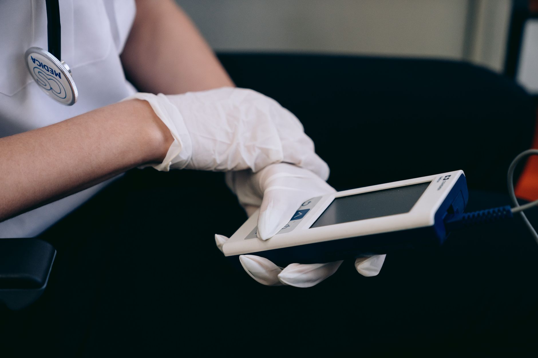 Healthcare worker with gloves using medical device indoors.