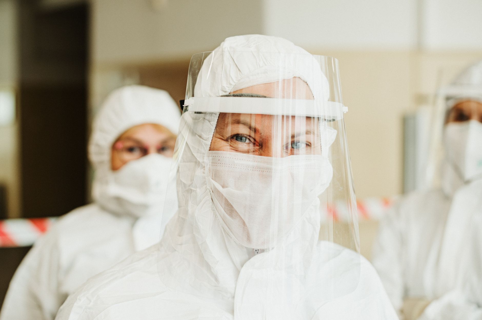 Healthcare workers wearing protective suits and face shields in hospital setting during pandemic.